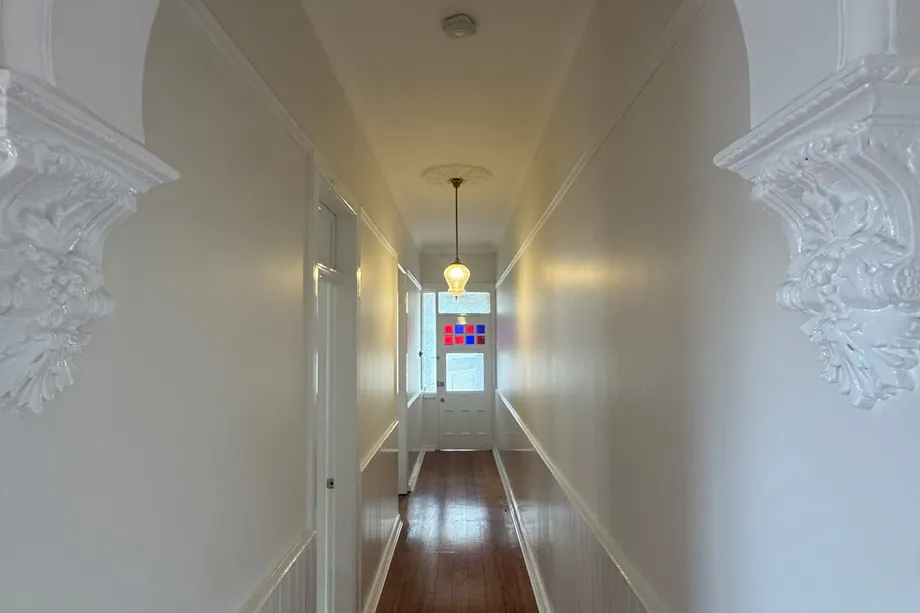 Long heritage hallway with white walls, ornate plaster arch corbels, a timber floor and a stained-glass front door