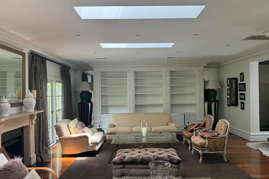 Formal living room with white walls, white built-in bookshelves, skylights, a fireplace and cream sofas