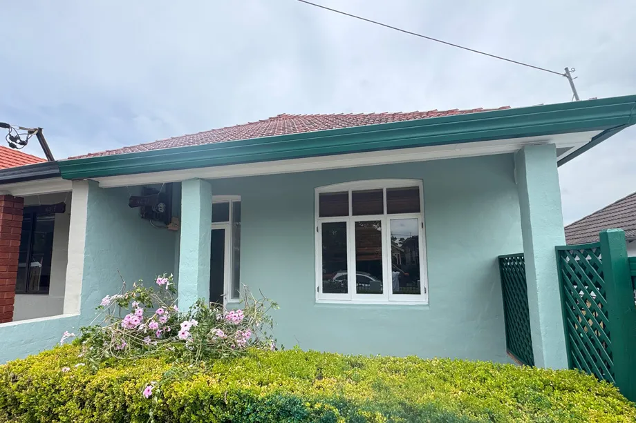 Bungalow front painted mint green with white window frames, teal gutters and a green lattice screen