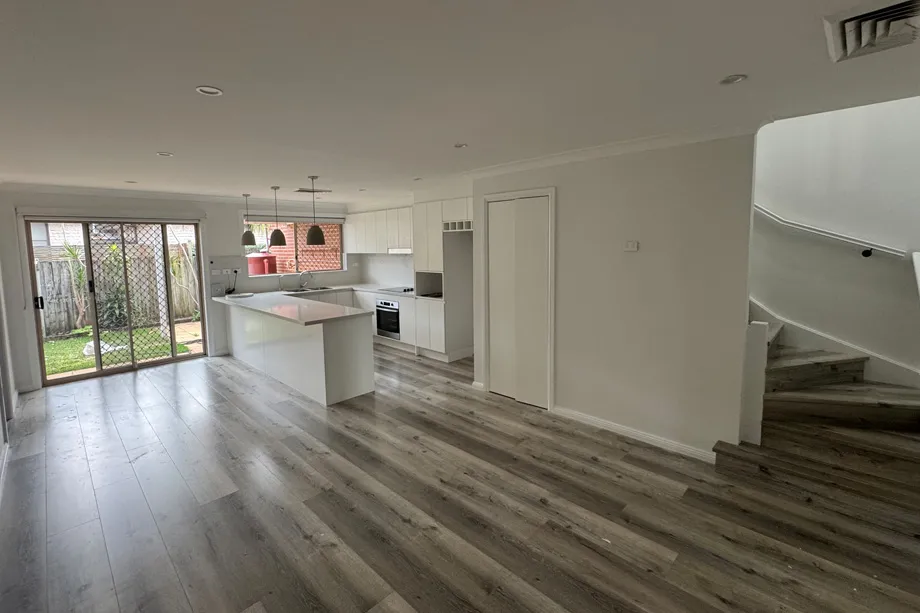 Open-plan living room and kitchen with white walls, a curved white staircase and sliding doors to the garden