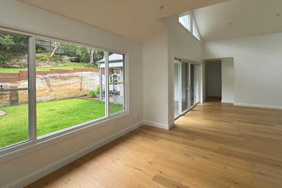 Living area with white walls, a raked ceiling, oak floor and a large window facing a sandstone garden