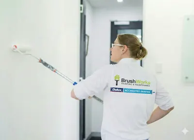 Painter in a Brushworks shirt using an extension roller on a white interior wall