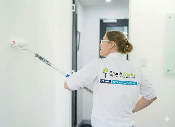 Painter in a Brushworks shirt using an extension roller on a white interior wall