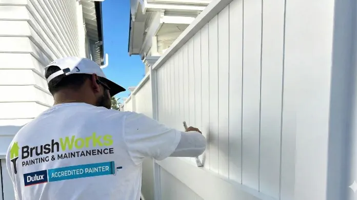 Brushworks painter brushing white paint onto vertical exterior weatherboards