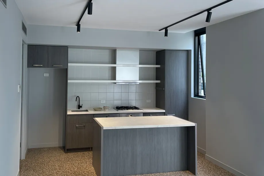Apartment kitchen with pale grey walls, dark timber-look cabinets, white open shelves and a stone-topped island