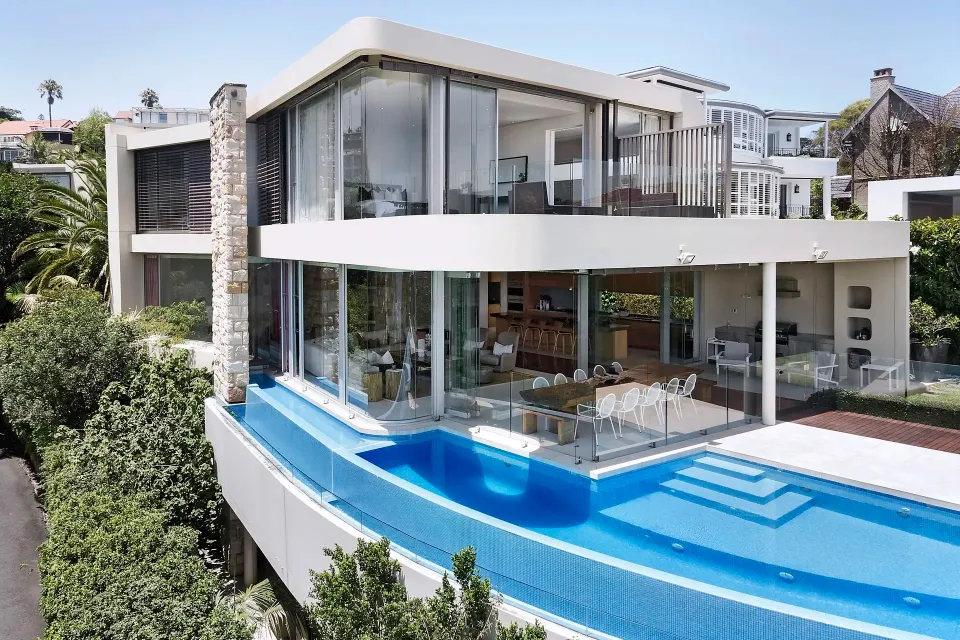 Two-storey white rendered house with a sandstone pillar, glass balconies and a blue infinity pool