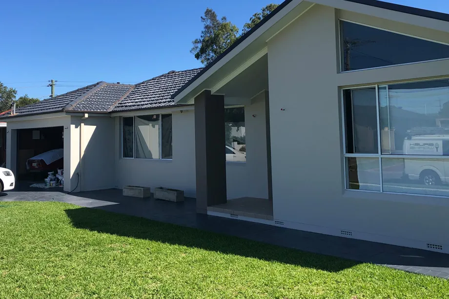 Single-storey house painted light grey with a charcoal feature pillar, a tiled roof and a green lawn
